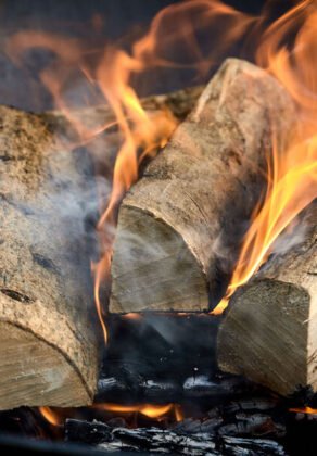 Recently lit fire with logs of flaming wood on a bed of chopped kindling in a portable summer barbecue in a close up panorama banner view